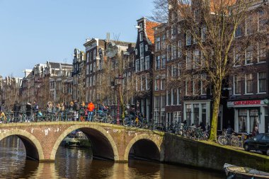 Amsterdam, Hollanda - 12 Mart 2016: Amstel Kanalı 'ndaki tekneler ve etrafta dolaşan insanlar. Amstel Kanalı üzerindeki köprü. Tipik Hollandalı evleri. Şehir görünümü.