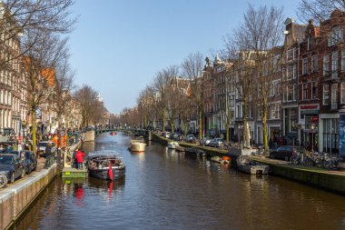 Amsterdam, Hollanda - 12 Mart 2016: Amstel Kanalı 'ndaki tekneler ve etrafta dolaşan insanlar. Amstel Kanalı üzerindeki köprü. Tipik Hollandalı evleri. Şehir görünümü.