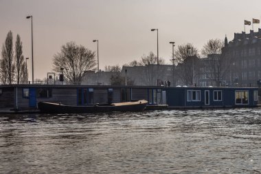 Amsterdam, Hollanda - 12 Mart 2016: Şehir merkezindeki kanalda konut mavnaları. Arka planda şık apartman cephesi var. Tipik Hollandalı evleri. Şehir görünümü.