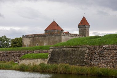 Estonya 'nın Saaremaa adasında hendek ve yeşilliklerle çevrili kırmızı çatılı kuleleri ve taş duvarları olan ortaçağ Kuressaare Kalesi.