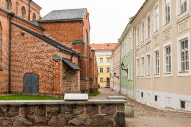 Tartu, Estonya 29 Ağustos 2021: Eski Tartu kasabasındaki kırmızı tuğlalı kilise ile pastel renkli tarihi binalar arasındaki dar kaldırım taşı caddesi.