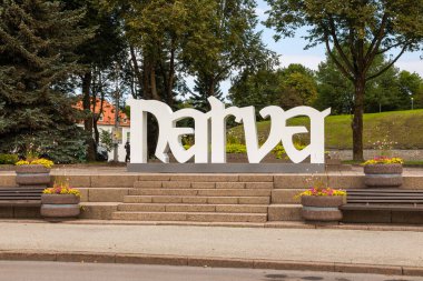 Narva, Estonya, 30 Ağustos 2021: Narva 'da çiçekler, ağaçlar ve kaldırımlarla döşenmiş bir park alanına yerleştirilmiş büyük beyaz şehir işareti.