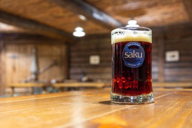 Lahemaa, Estonya, 31 Ağustos 2021: Lahemaa Milli Parkı 'ndaki kırsal bir meyhanenin içindeki ahşap bir masaya koyu bir bardak Saku birası yerleştirildi.