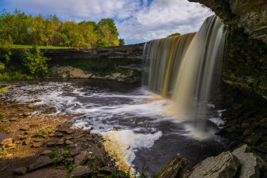 Estonya 'daki Lahemaa Ulusal Parkı' ndaki bir nehir havuzuna düşen kayalık bir uçurumdan düşen perde tarzı şelale..