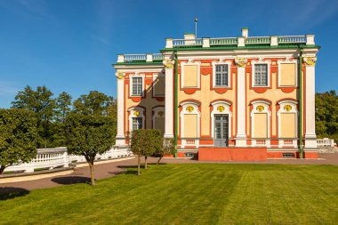 Estonya 'nın Tallinn kentinde renkli çiçek tarhları olan resmi bir bahçenin arkasında bir barok sarayı duruyor. Güneş ışığı süslemeleri ve manzaralı alanları aydınlatır..
