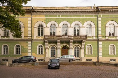 Tallinn, Estonya 2 Eylül 2021: Kemerli camlı tarihi yeşil bir bina park halindeki çok sayıda arabalı bir kaldırım taşı alan boyunca duruyor.