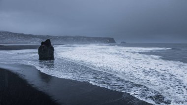 Dalgalar İzlanda 'da Vik i Myrdal yakınlarındaki kara kumsal kıyılarını siler. Bazalt deniz yığını ve uzak uçurumlar kış kıyı şeridinde yükseliyor..