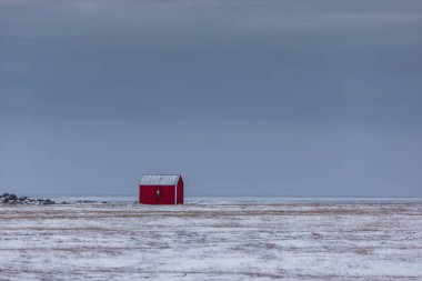 İzlanda 'da Krysuvik yakınlarında geniş bir kar tarlasında küçük kırmızı bir kulübe tek başına duruyor. Alçak bulutlar açık arazide sessiz bir kış atmosferi yaratır..
