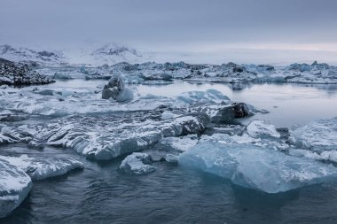 İzlanda 'daki Jokulsarlon Buzul Gölü' nde yüzen buzdağları, karla kaplı dağlar ve sakin buzul suyuyla çevrili..