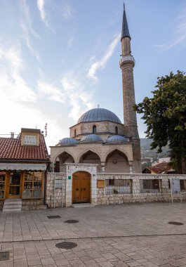 Saraybosna, Bosna-Hersek: 15 Ağustos 2022: Saraybosna 'daki geleneksel dükkanlar ve cami minaresiyle eski kent caddesinin manzarası ve arka planda dağlar ve sakin kentsel atmosfer.