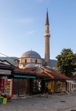 Saraybosna, Bosna-Hersek: 15 Ağustos 2022: Saraybosna 'daki geleneksel dükkanlar ve cami minaresiyle eski kent caddesinin manzarası ve arka planda dağlar ve sakin kentsel atmosfer.