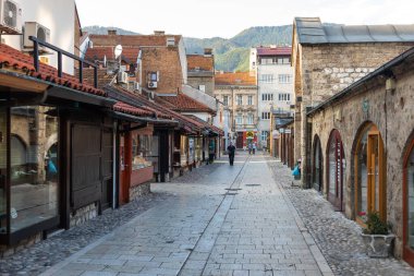 Saraybosna, Bosna-Hersek 15 Ağustos 2022: Eski Saraybosna kentinde geleneksel dükkanlar ve taş binalarla dolu dar bir sokak, Osmanlı mimarisi ve günlük şehir yaşamını yansıtıyor.