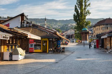 Saraybosna, Bosna-Hersek 15 Ağustos 2022: Arkasında tarihi bir cami ve minare bulunan Bascarsija eski kasabasındaki sokak kafeleri ve geleneksel restoranlar.