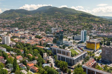 Saraybosna, Bosna-Hersek: 15 Ağustos 2022: Çağdaş ofis kuleleri, yerleşim bölgeleri ve arka planda yeşil tepeler bulunan Saraybosna şehir merkezinin panoramik hava manzarası.