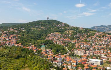 Saraybosna, Bosna-Hersek: 15 Ağustos 2022: Çağdaş ofis kuleleri, yerleşim bölgeleri ve arka planda yeşil tepeler bulunan Saraybosna şehir merkezinin panoramik hava manzarası.