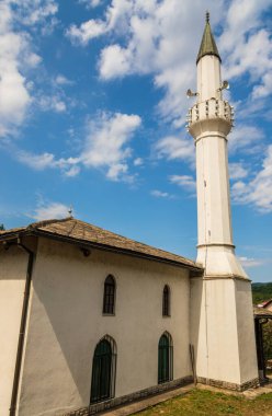 Bosna-Hersek 'in Konjiç kentindeki ağaçlar ve yerleşim alanlarıyla çevrili yüksek minareli cami binası.