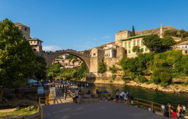 Bosna-Hersek 'in Mostar kenti 16 Ağustos 2022: Eski Mostar kentindeki UNESCO Dünya Mirası Alanı olan tarihi Stari Most köprüsünün altındaki Neretva Nehri boyunca toplanan insanlar.