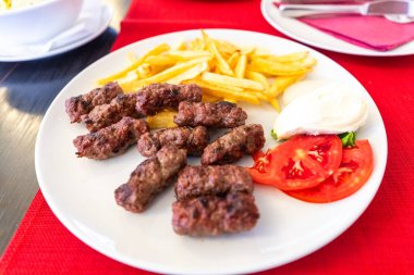 Bosna-Hersek 'ten ünlü bir geleneksel Balkan yemeği olan Cevapi eti, kızarmış patates kızartması ve taze doğranmış domateslerle servis ediliyor.
