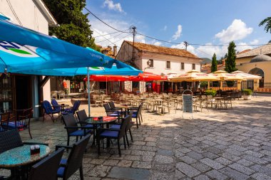 Trebinje, Bosna ve Hercegovina - 20 Ağustos 2022: Trebinje 'de açık kafeterya masaları ve renkli şemsiyeler altında sandalyeler.