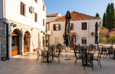 Trebinje, Bosna ve Hercegovina - 21 Ağustos 2022: Eski taş binalar ve açık kafeler minareli sakin bir kaldırım kaldırımı hattı.