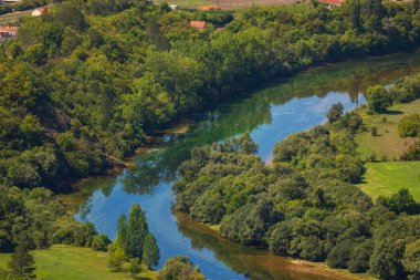 Virajlı Trebisnjica nehri, Bosna-Hersek 'in Trebinje kentinde yemyeşil ağaçları, yemyeşil vadileri ve uzak evleri yansıtıyor.