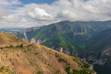 Lukomir, Konjiç, Bosna-Hersek yakınlarında engebeli dağ zirveleri ve bulutlu gökyüzünün altında yemyeşil bir orman vadisi manzaralı yürüyüş manzarası.