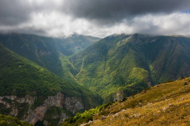 Yoğun bulutlar ve atmosfer ışığı altında derin bir vadiyi tanımlayan yemyeşil yamaçlar, Bosna-Hersek 'in Lukomir kentindeki güzel doğal manzarayı gösteriyor.