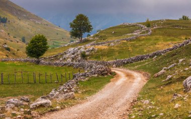 Bosna-Hersek 'in Konjiç kentinde geleneksel kuru taş duvarlarla çevrili yeşil çayırlar ve kayalık tepelerden geçen toprak yol.