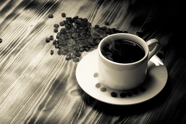 Кофейные зерна и кофе в белой чашке на деревянном столе. Селективный — стоковое фото