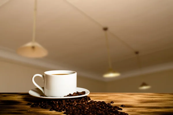 Caffè in una tazza sul tavolo in legno di fronte a un interio sfocato — Foto Stock