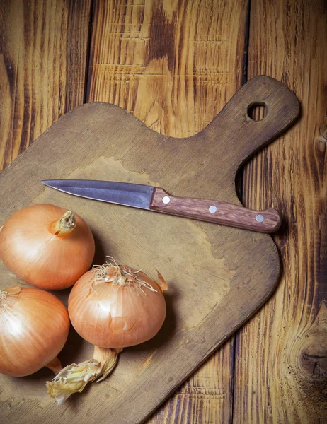 Oignon frais et planche à découper rétro sur une vieille table en bois brûlé o — Photo