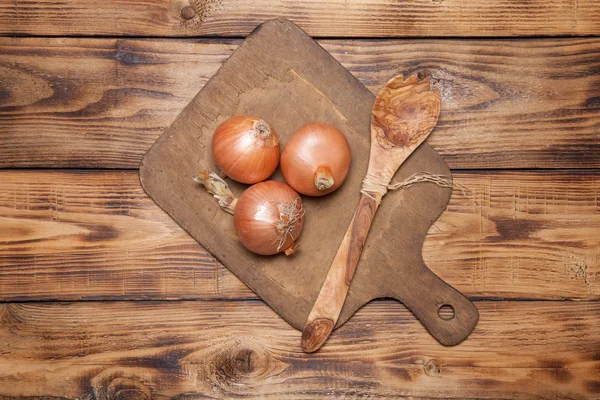 Frische Zwiebel und Retro-Schneidebrett auf altem Holztisch — Stockfoto
