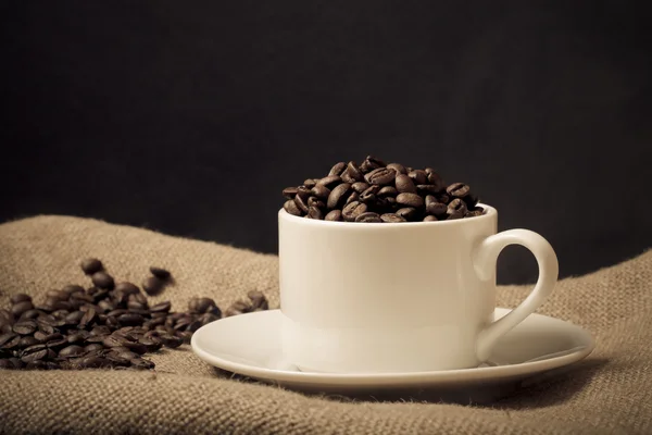カップ、ソーサー、黄麻布の背景にコーヒー豆。選択的な f — ストック写真