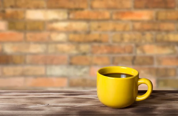 Kaffee in gelber Tasse auf Holztisch gegenüber einem defokussierten Ziegelstein — Stockfoto