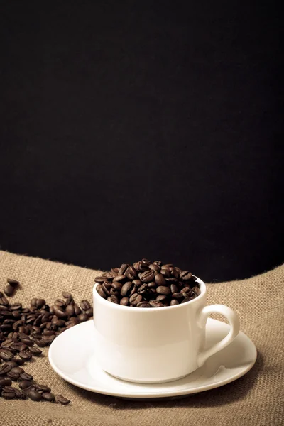 Copa, platillo y granos de café sobre un fondo de arpillera. Tonificado — Foto de Stock