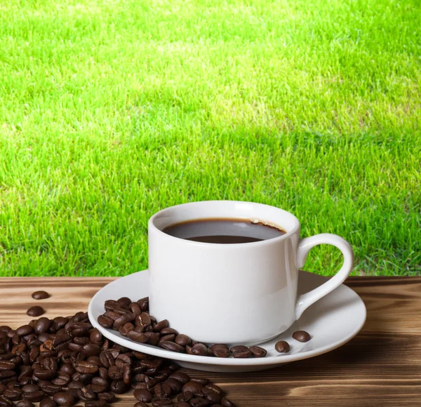 Кофейные зерна и кофе в белой чашке на деревянном столе напротив — стоковое фото