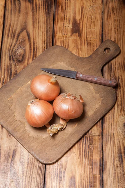 Cebola fresca e placa de corte retro na velha mesa queimada de madeira o — Fotografia de Stock