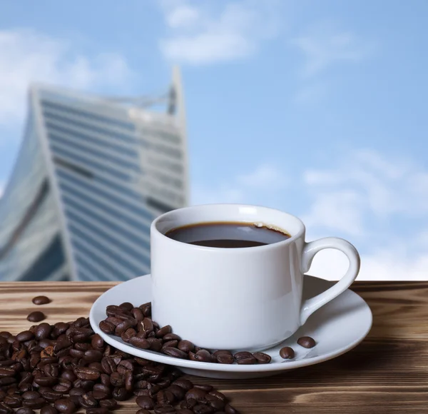 Granos de café y café en taza blanca en la mesa de madera frente a un — Foto de Stock