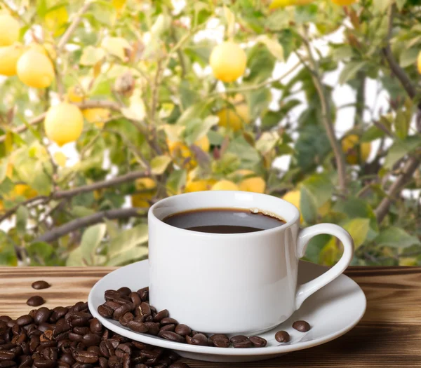 Kaffebønner og kaffe i hvid kop på træbord overfor en - Stock-foto