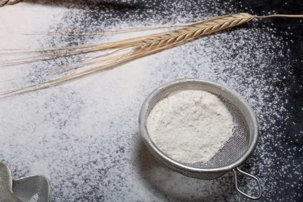 Wheat ears, baking forms, sieve and sprinkle flour on black back — Stock Photo, Image