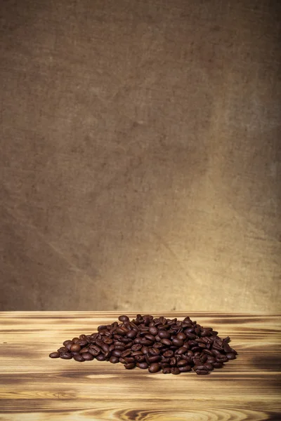 Montón de granos de café en la mesa de madera frente a una arpillera desenfocada —  Fotos de Stock