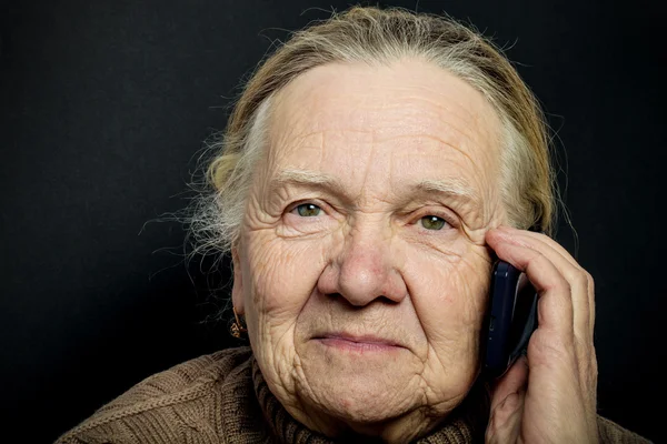 Портрет пожилой женщины с телефоном на темном фоне. Тон — стоковое фото
