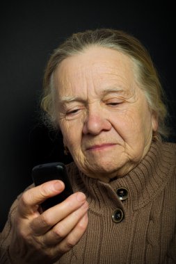 Yaşlı kadın koyu arka plan üzerinde telefon ile portresi. Ton