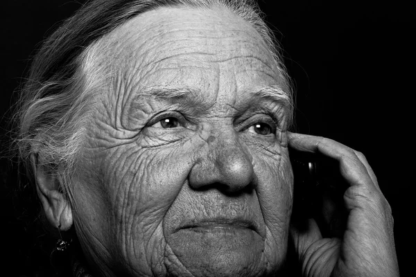 Retrato de mulher idosa com telefone em fundo escuro. Tonelada — Fotografia de Stock