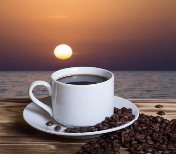 Kaffeebohnen und Kaffee in weißer Tasse auf Holztisch gegenüber — Stockfoto