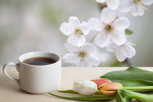 Kawa w filiżance i tulipany na drewnianym stole naprzeciwko rozmyte — Zdjęcie stockowe