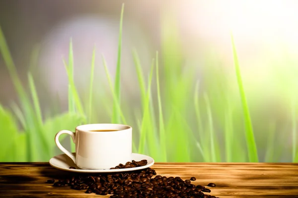 Granos de café y café en taza blanca en la mesa de madera frente a un — Foto de Stock