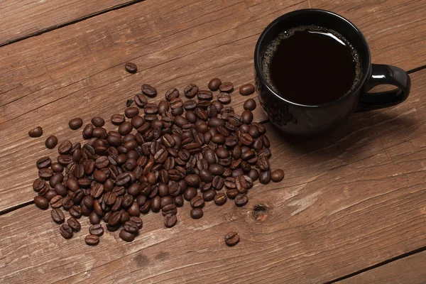 Schwarze Tasse Kaffee und Kaffeesamen auf altem Holztisch — Stockfoto