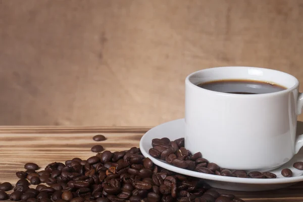 Granos de café y café en taza blanca en la mesa de madera frente a un — Foto de Stock