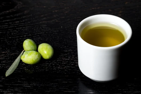 Bayas de oliva verdes y tapa de aceite de oliva fresco sobre una madera negra —  Fotos de Stock